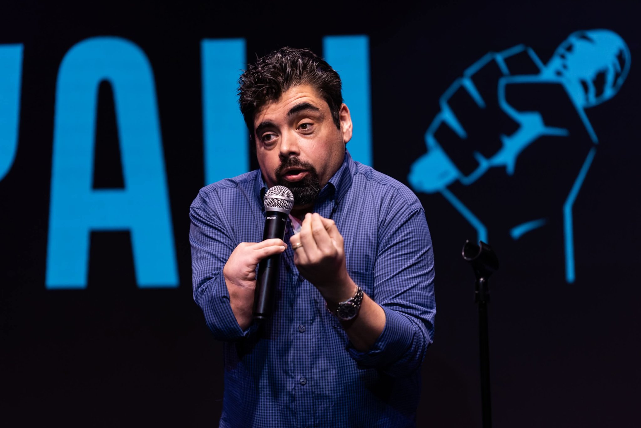 Photo of Michael Beers, a man with dark hair and facial hair, holding a microphone and speaking on a stage.
