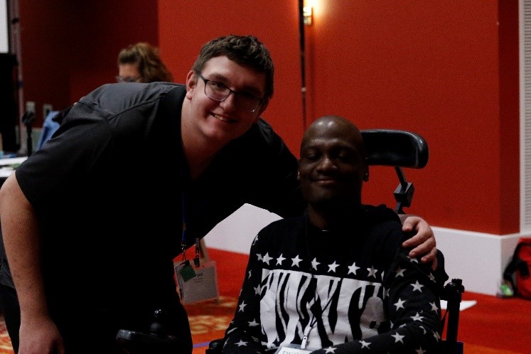 Two men one standing one setting in a wheelchair