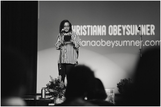 ChrisTiana ObeySumner standing on a stage holding a microphone