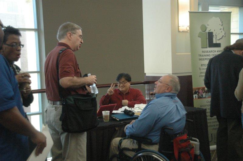 2 men at the exhibits and Exhibitor is sharing the peace sign with photographer