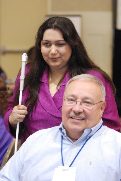 lady with white cane standing over a man sitting in front of her.